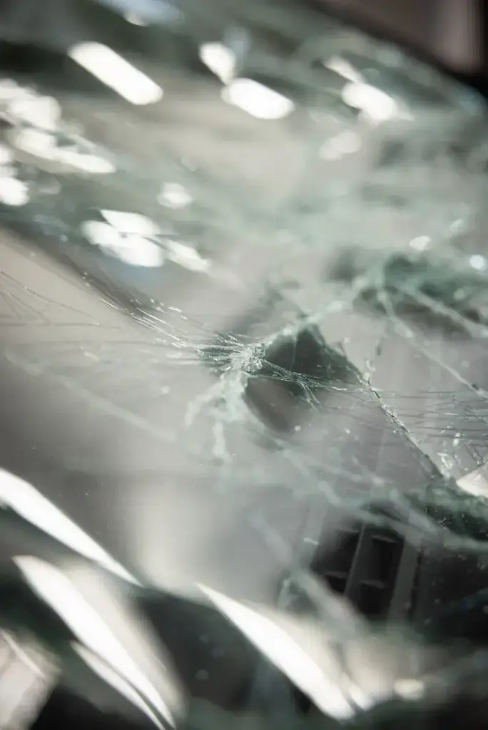 Nahaufnahme einer beschädigten Autoscheibe mit sichtbaren Rissen und Glasbruchstrukturen unter Innenlicht.