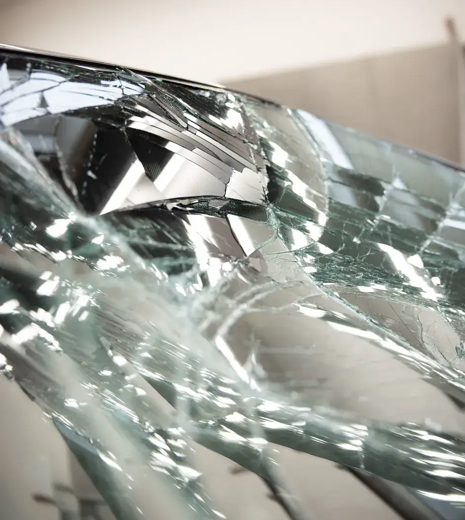 Nahaufnahme einer zerstörten Windschutzscheibe mit starkem Rissbruch und Lichtreflexionen – typischer Fall für Autoglas-Austausch bei Karosserie Blanke.
