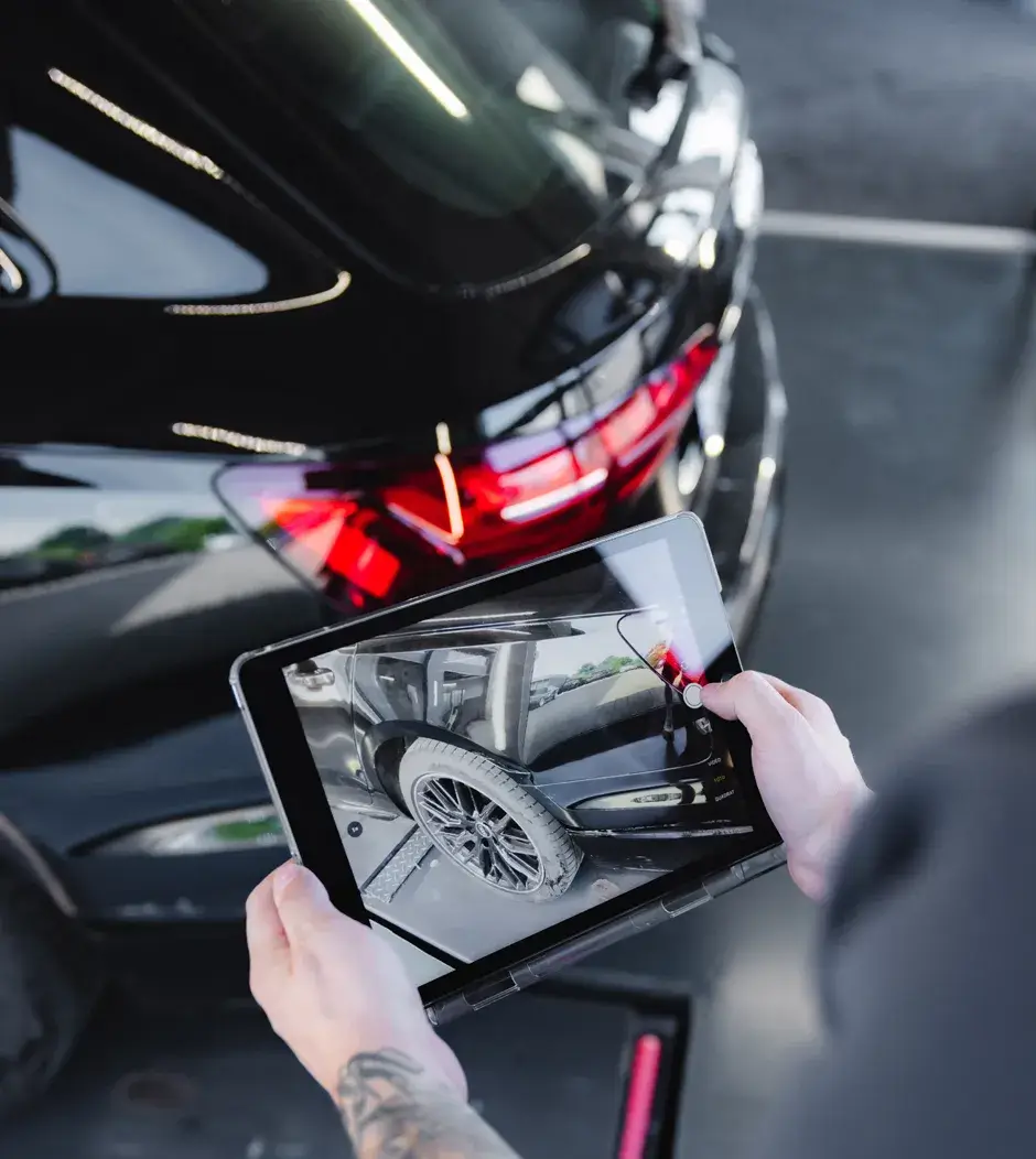 Ein Mitarbeiter dokumentiert mit einem Tablet einen Unfallschaden an einem schwarzen Fahrzeug - moderne Schadensaufnahme bei Karosserie Blanke.