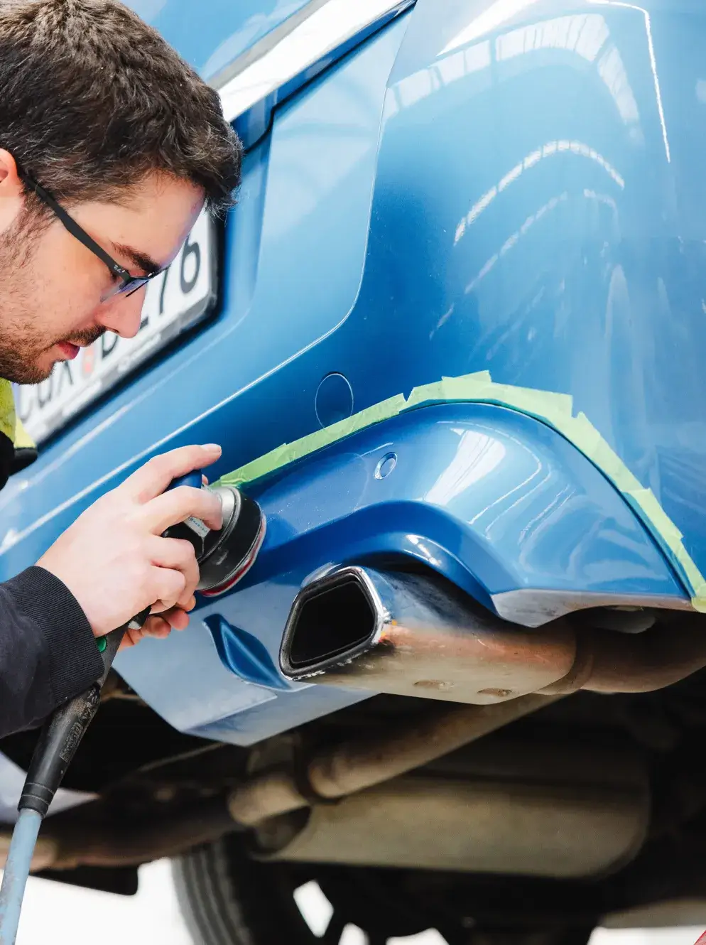 Ein Mitarbeiter poliert den hinteren Stoßfänger eines blauen Fahrzeugs nach der Lackierung - Karosserie Blanke Bremerhaven