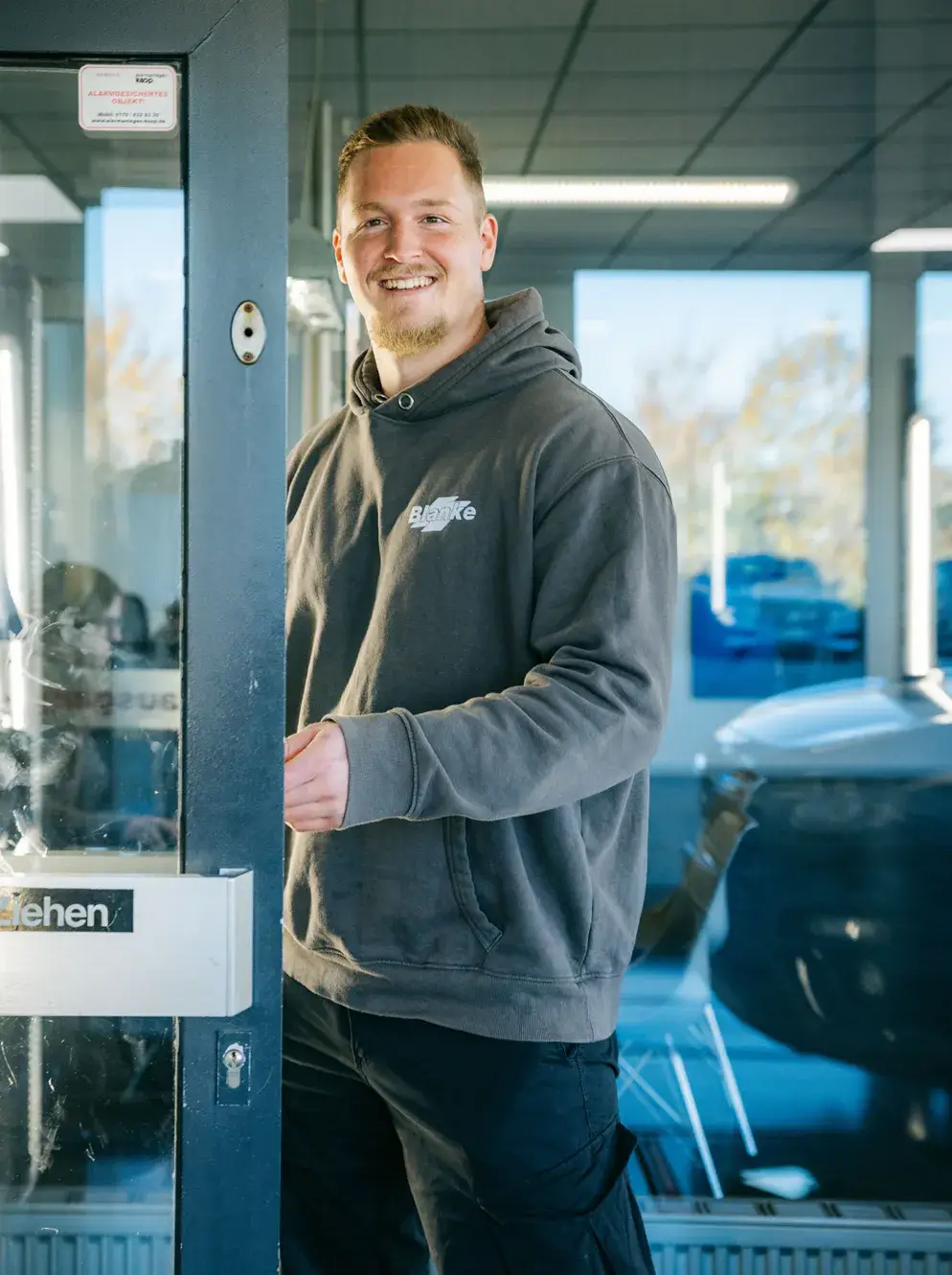 Ein Mitarbeiter von Karosserie Blanke öffnet freundlich die Tür für einen Kunden im Empfangsbereich der Werkstatt.