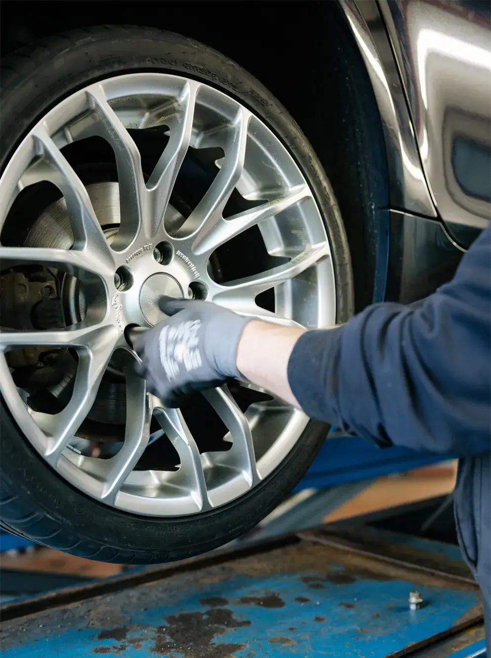 Ein Mitarbeiter montiert ein Leichtmetallrad an einem Fahrzeug auf der Hebebühne - Reifenservice bei Karosserie Blanke.