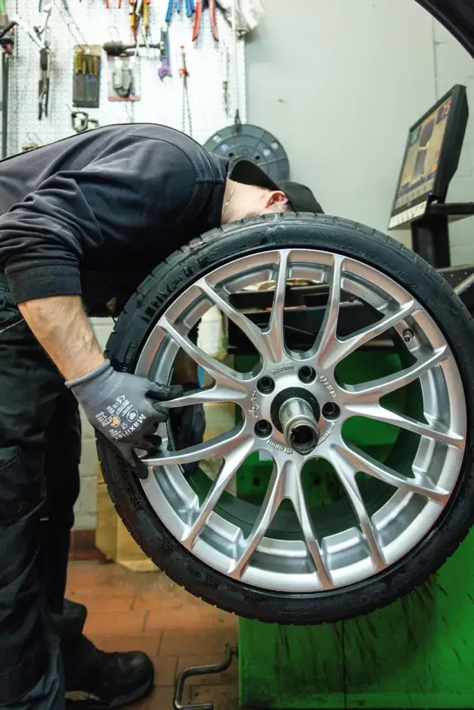 Ein Mitarbeiter wuchtet einen montierten Reifen mit einer elektronischen Wuchtmaschine in der Werkstatt von Karosserie Blanke aus.