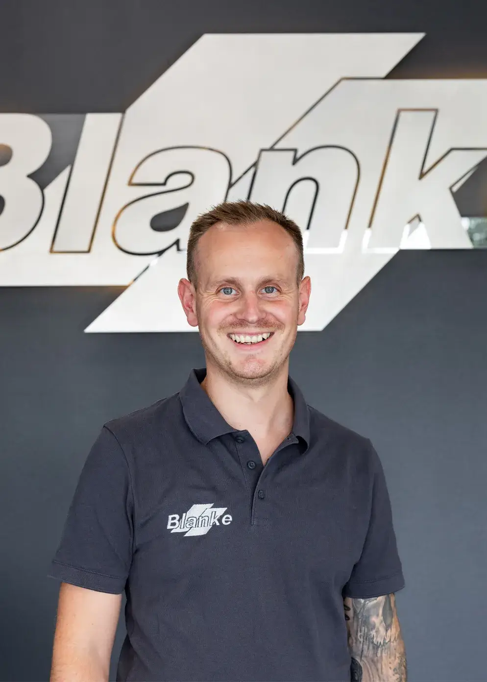 Porträt von Stephen Tirre dem Geschäftsführer von Karosserie Blanke vor dem Firmenlogo im Empfangsbereich.